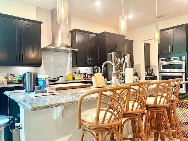 16611 Toccoa Row, Winter Garden, FL 34787 - kitchen featuring wall chimney range hood, stainless steel appliances, backsplash, a kitchen breakfast bar, and decorative light fixtures