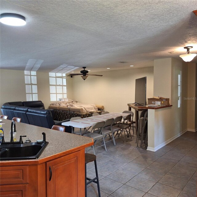 10012 Lake Louisa Rd, Clermont, FL 34711 - kitchen featuring a sink, a breakfast bar area, dark tile patterned floors, brown cabinets, and a textured ceiling