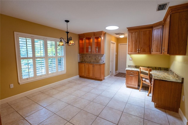 1550 Kevin Ln, Deland, FL 32724 - kitchen with brown cabinetry, glass insert cabinets, a chandelier, light tile patterned flooring, and light stone countertops