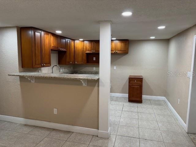2847 W Harwood St Unit 0, Orlando, FL 32805 - kitchen featuring light stone counters, a breakfast bar area, recessed lighting, brown cabinets, and light tile patterned floors