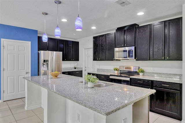 144 Williamson Dr, Davenport, FL 33897 - kitchen with appliances with stainless steel finishes, light tile patterned flooring, dark cabinetry, hanging light fixtures, and a sink