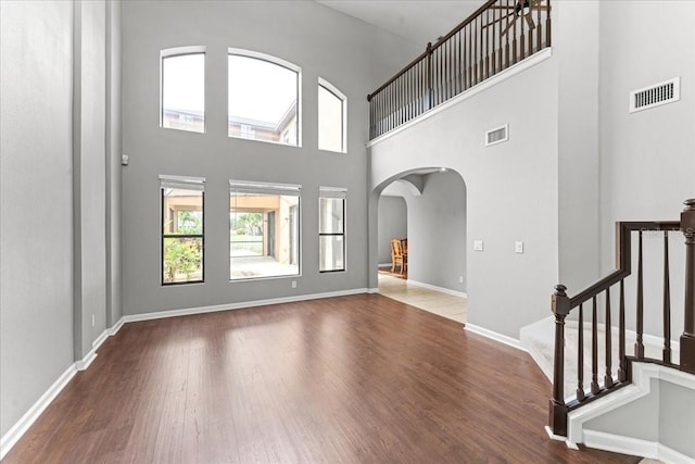 2753 Glenridge Cir, Merritt Island, FL 32953 - unfurnished living room featuring arched walkways, a towering ceiling, wood finished floors, baseboards, and stairway