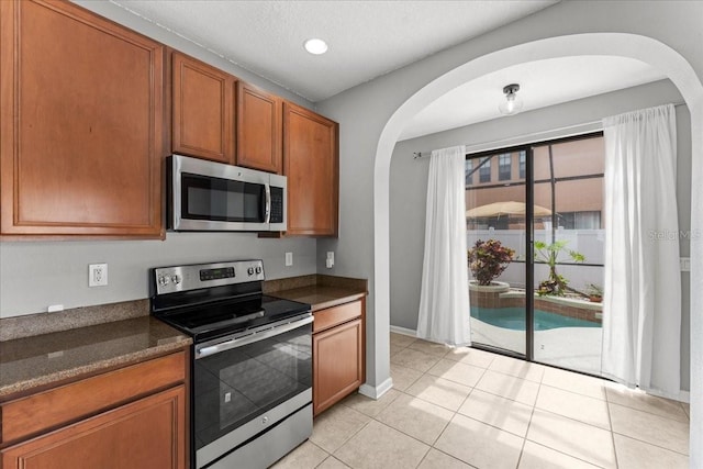 2753 Glenridge Cir, Merritt Island, FL 32953 - kitchen featuring stainless steel appliances, arched walkways, brown cabinetry, light tile patterned floors, and baseboards