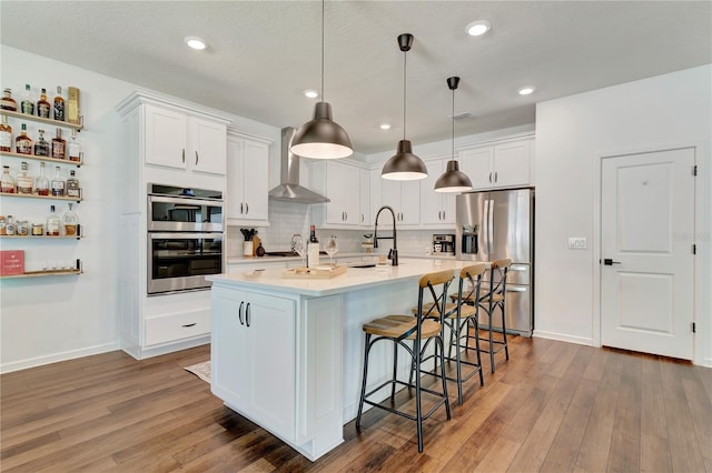 2335 Green Symphony Pl, Oviedo, FL 32765 - kitchen with appliances with stainless steel finishes, wall chimney range hood, white cabinets, wood finished floors, and recessed lighting
