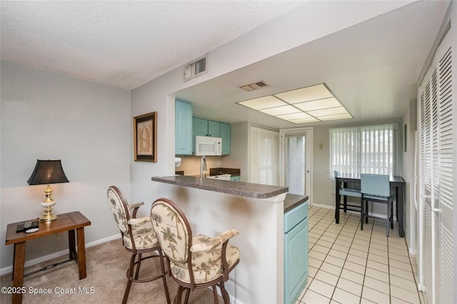 1515 Huntington Ln Unit 426, Rockledge, FL 32955 - kitchen with white microwave, blue cabinetry, dark countertops, a kitchen bar, and a peninsula