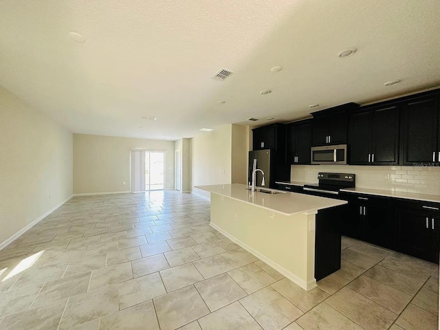 2807 Alder Berry Blvd, Ocoee, FL 34761 - kitchen with stainless steel microwave, dark cabinetry, black / electric stove, a center island with sink, and a sink
