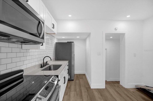 906 Kensington Dr, Orlando, FL 32808 - kitchen with stainless steel appliances, a sink, decorative backsplash, light wood-style flooring, and white cabinets