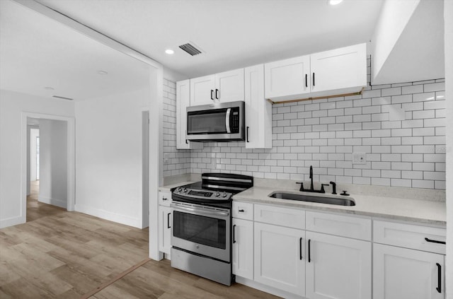 906 Kensington Dr, Orlando, FL 32808 - kitchen featuring appliances with stainless steel finishes, a sink, white cabinets, tasteful backsplash, and baseboards
