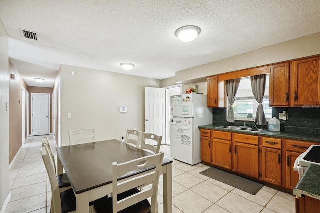 6663 NW 60th St, Ocala, FL 34482 - kitchen with freestanding refrigerator, brown cabinetry, a sink, light tile patterned floors, and a textured ceiling