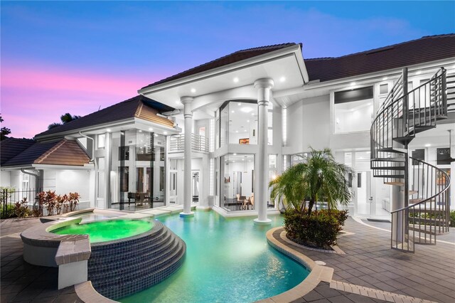 9138 Great Heron Cir, Orlando, FL 32836 - back of property at dusk featuring stairway, a patio, a pool with connected hot tub, a tile roof, and stucco siding