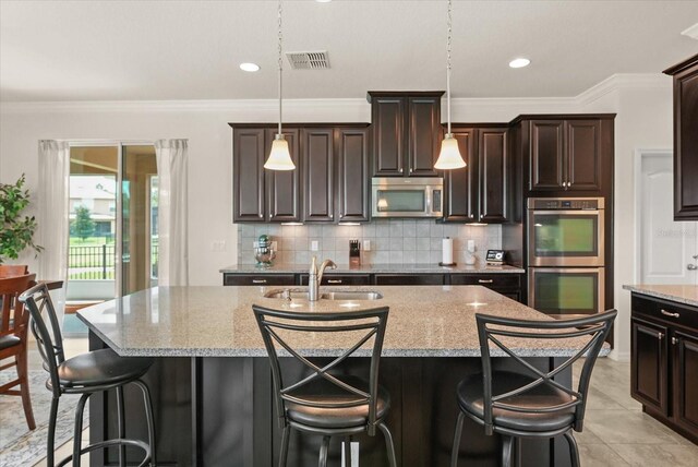 1613 Water Elm Ct, Orlando, FL 32825 - kitchen with appliances with stainless steel finishes, a sink, tasteful backsplash, a center island with sink, and light stone countertops