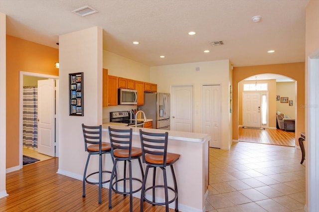 4642 Waterside Pointe Cir, Orlando, FL 32829 - kitchen with stainless steel appliances, arched walkways, a kitchen breakfast bar, a peninsula, and brown cabinets