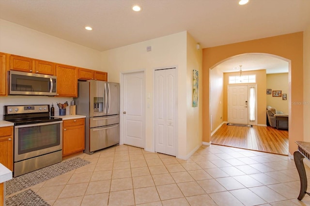 4642 Waterside Pointe Cir, Orlando, FL 32829 - kitchen with appliances with stainless steel finishes, arched walkways, brown cabinetry, light tile patterned floors, and recessed lighting