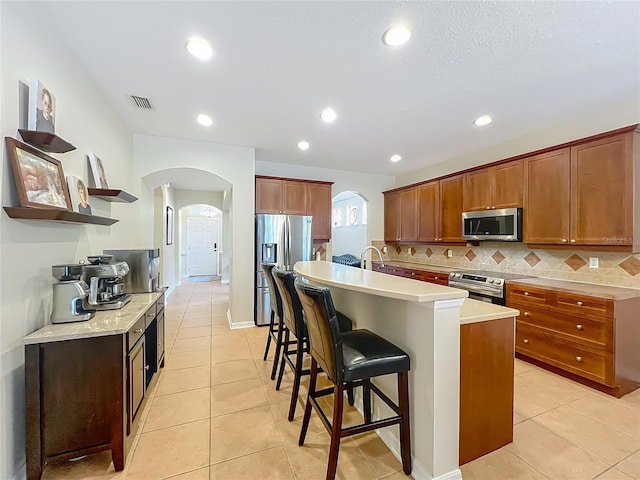 12641 Arley Dr, Windermere, FL 34786 - kitchen with appliances with stainless steel finishes, arched walkways, light tile patterned floors, open shelves, and a breakfast bar