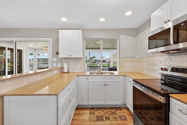 24277 Treasure Island Blvd, Punta Gorda, FL 33955 - kitchen with appliances with stainless steel finishes, a peninsula, backsplash, light wood-style flooring, and white cabinets