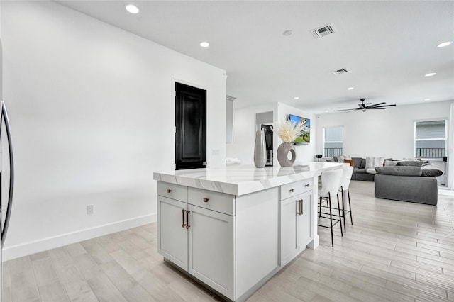 5609 Zestar Ln, Loxahatchee, FL 33470 - kitchen with a kitchen island, light wood finished floors, ceiling fan, a kitchen breakfast bar, and light stone countertops