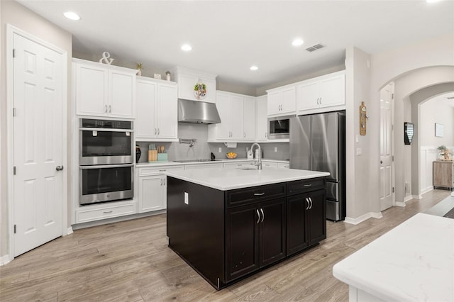 1113 Fieldstone Cir, Oviedo, FL 32765 - kitchen with appliances with stainless steel finishes, under cabinet range hood, dark cabinets, arched walkways, and light countertops