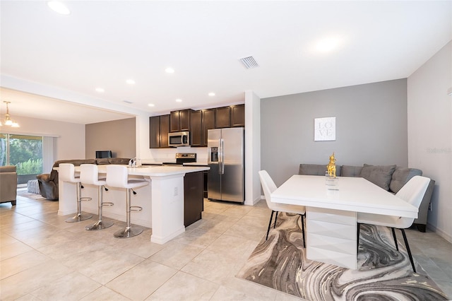 110 Claire Ln, Davenport, FL 33837 - kitchen featuring appliances with stainless steel finishes, open floor plan, a breakfast bar area, an island with sink, and dark brown cabinetry