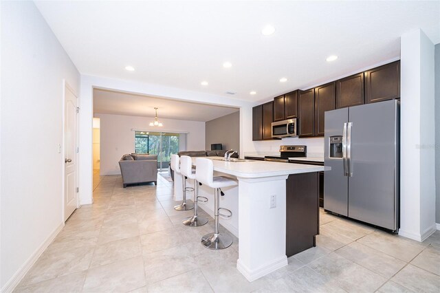 110 Claire Ln, Davenport, FL 33837 - kitchen featuring appliances with stainless steel finishes, dark brown cabinets, light countertops, a center island with sink, and a kitchen bar