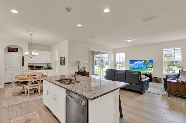 kitchen with dishwasher, a sink, light wood-style floors, a center island with sink, and light stone countertops
