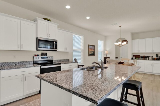 kitchen featuring stainless steel appliances, a sink, recessed lighting, a kitchen bar, and light wood-style floors