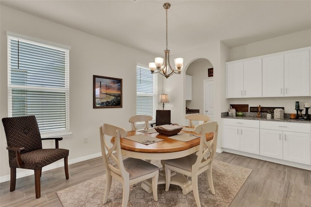 dining space featuring light wood-style floors, arched walkways, a chandelier, and baseboards