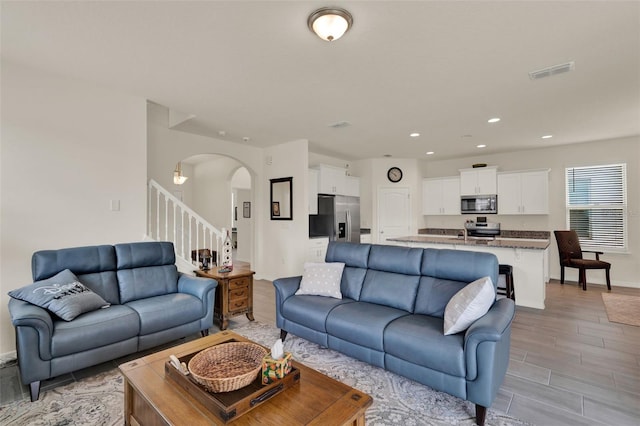 living area with arched walkways, light wood finished floors, recessed lighting, stairway, and baseboards