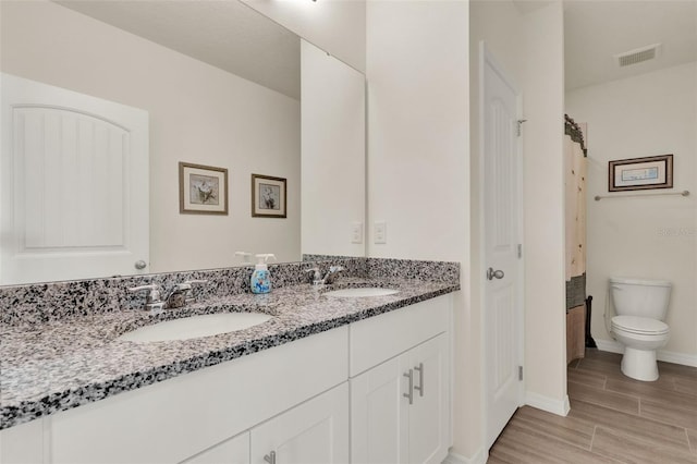 bathroom featuring double vanity, toilet, wood finished floors, and baseboards