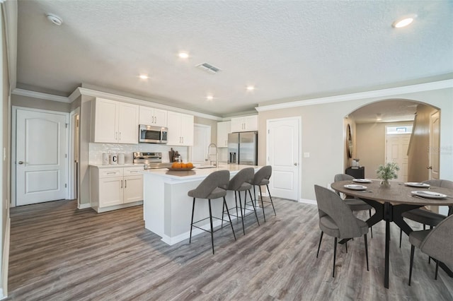 129 Eagleview Loop, Davenport, FL 33837 - kitchen with appliances with stainless steel finishes, arched walkways, a center island with sink, wood finished floors, and a kitchen breakfast bar