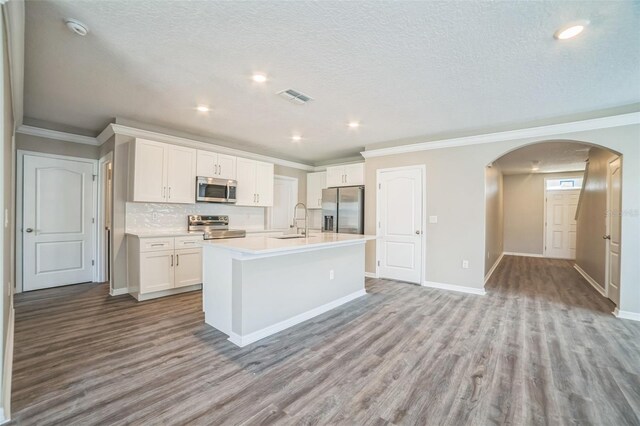 129 Eagleview Loop, Davenport, FL 33837 - kitchen with appliances with stainless steel finishes, arched walkways, wood finished floors, a kitchen island with sink, and ornamental molding