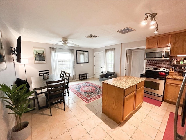 312 W Hull Ave, Oakland, FL 34760 - kitchen featuring stainless steel appliances, brown cabinetry, light tile patterned floors, a center island, and decorative backsplash