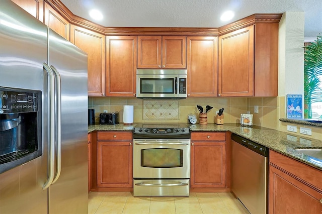 7616 Cabana Ct Unit 301, Reunion, FL 34747 - kitchen with stainless steel appliances, dark stone counters, decorative backsplash, and brown cabinets
