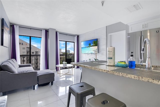 6165 Carrier Dr Unit 2605, Orlando, FL 32819 - kitchen with white cabinetry, a kitchen bar, light stone countertops, open floor plan, and stainless steel fridge