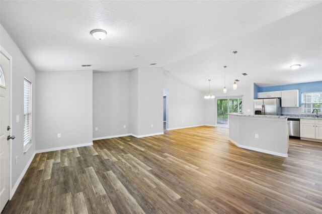 395 Alcazar Ave, De Leon Springs, FL 32130 - unfurnished living room featuring wood finished floors, healthy amount of natural light, baseboards, lofted ceiling, and a chandelier