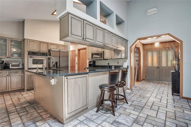 616 Magnolia St, Windermere, FL 34786 - kitchen featuring appliances with stainless steel finishes, a towering ceiling, brick patterned flooring, a kitchen breakfast bar, and glass insert cabinets