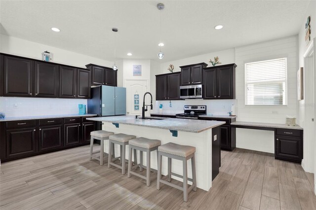 15613 Camp Dubois Cres, Winter Garden, FL 34787 - kitchen featuring appliances with stainless steel finishes, a sink, light wood finished floors, decorative backsplash, and a kitchen breakfast bar