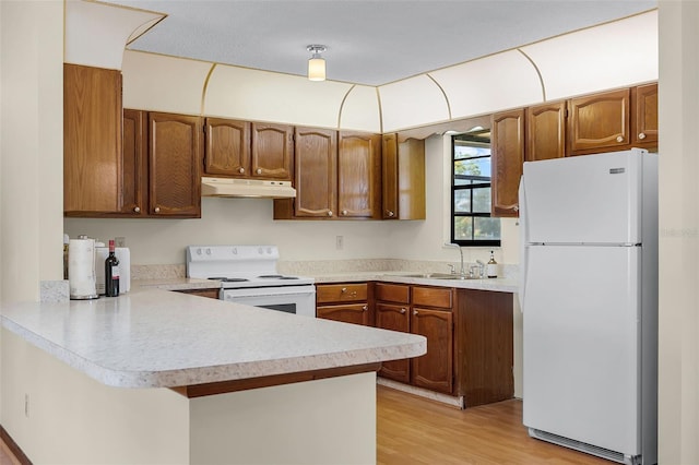 281 NE Greenbrier Ave, Port St Lucie, FL 34983 - kitchen with white appliances, under cabinet range hood, a peninsula, light countertops, and light wood-style flooring