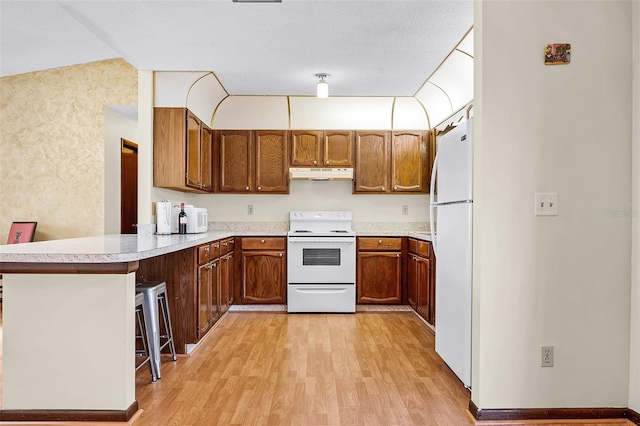 281 NE Greenbrier Ave, Port St Lucie, FL 34983 - kitchen featuring white appliances, under cabinet range hood, light wood-style flooring, a peninsula, and brown cabinetry