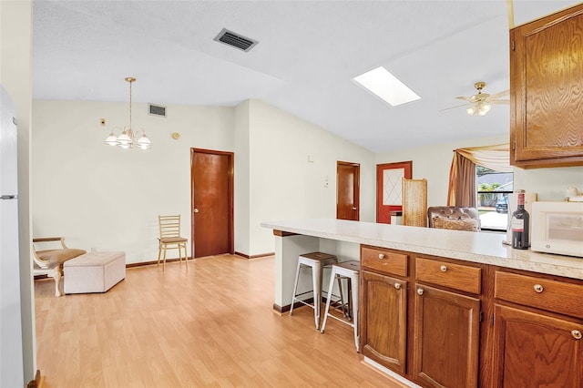 281 NE Greenbrier Ave, Port St Lucie, FL 34983 - kitchen with lofted ceiling, white microwave, a peninsula, light wood-style flooring, and brown cabinets