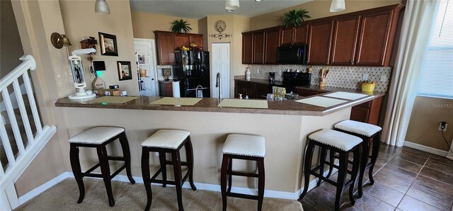 7620 Tangle Rush Dr, Gibsonton, FL 33534 - kitchen with black appliances, a kitchen breakfast bar, decorative backsplash, a peninsula, and dark brown cabinets