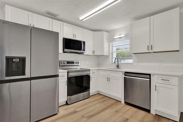 324 James Pl, Saint Cloud, FL 34769 - kitchen with stainless steel appliances, a sink, light wood-style floors, white cabinets, and light countertops