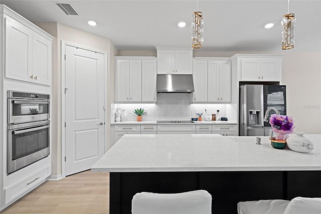 7163 Talamore Dr, Wesley Chapel, FL 33545 - kitchen with under cabinet range hood, appliances with stainless steel finishes, light wood-style floors, a kitchen breakfast bar, and backsplash