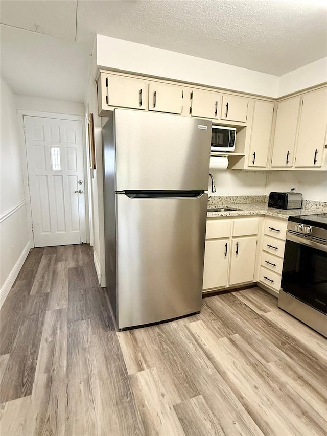 10301 US Highway 27 Unit 34, Clermont, FL 34711 - kitchen featuring appliances with stainless steel finishes, a sink, light wood-style flooring, a textured ceiling, and cream cabinets