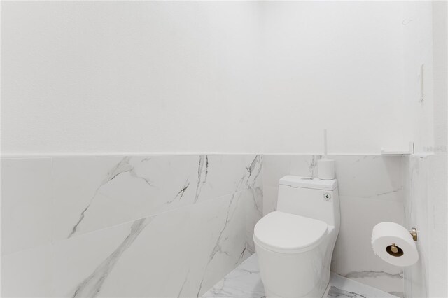 10001 Newington Dr, Orlando, FL 32836 - bathroom featuring marble look tile flooring, toilet, tile walls, and a wainscoted wall