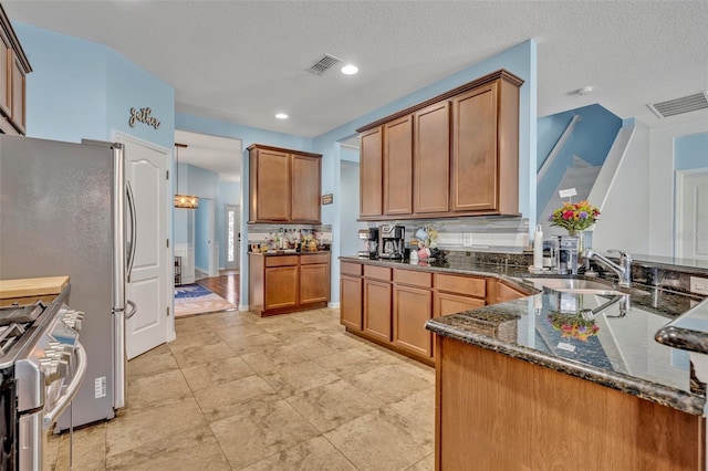 11616 Thacker Dr, Clermont, FL 34711 - kitchen featuring stainless steel gas range oven, dark stone counters, brown cabinetry, a textured ceiling, and a peninsula