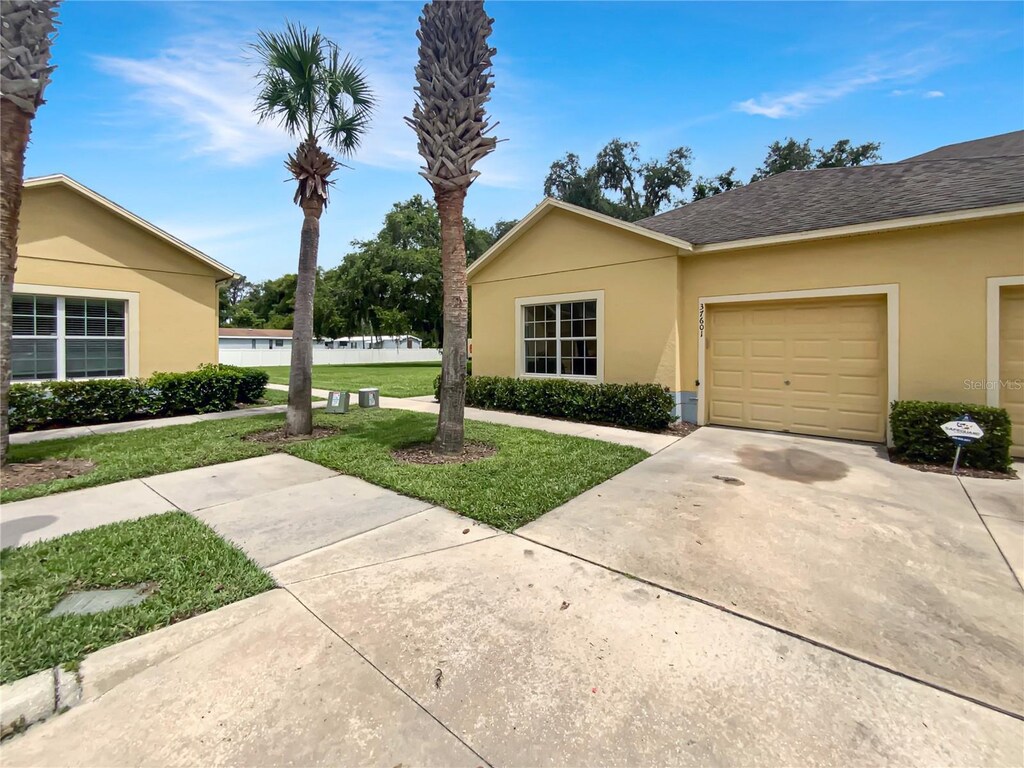 37601 Georgina Ter, Zephyrhills, FL 33542 - view of front of house featuring a front yard, stucco siding, an attached garage, and roof with shingles