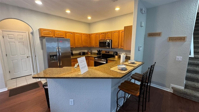 16631 Lazy Breeze Loop, Clermont, FL 34714 - kitchen with stainless steel appliances, a kitchen breakfast bar, wood finished floors, a peninsula, and brown cabinetry