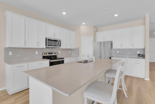 7639 Agrigento St, Clermont, FL 34714 - kitchen featuring stainless steel appliances, backsplash, light wood-type flooring, a center island with sink, and white cabinets