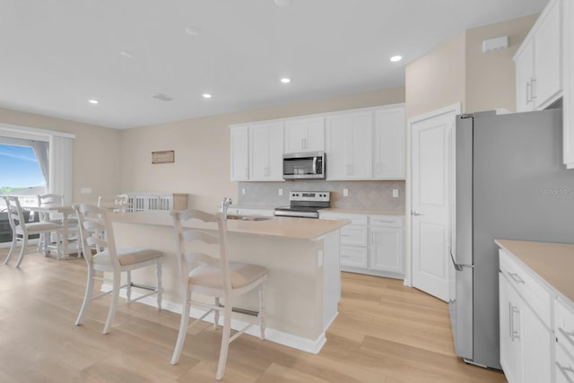 7639 Agrigento St, Clermont, FL 34714 - kitchen featuring appliances with stainless steel finishes, light wood finished floors, a kitchen bar, white cabinets, and recessed lighting