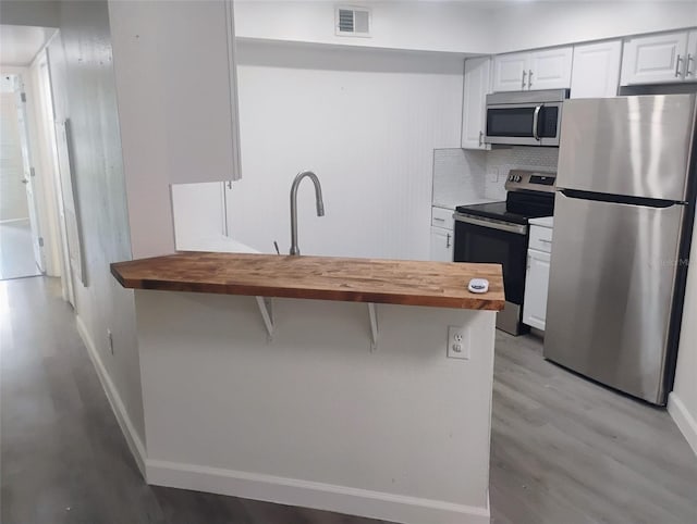 4674 Pembrook Pl Unit J 101, Orlando, FL 32811 - kitchen with stainless steel appliances, wood counters, light wood-style floors, white cabinetry, and tasteful backsplash